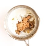 A saucepan filled with melted butter and a heap of brown sugar, viewed from above on a white background.