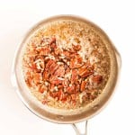 A stainless steel saucepan containing melted butter and chopped pecans on a white background.