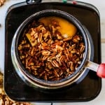 A saucepan with chopped pecans, butter, eggs, and brown sugar sits on a black stovetop—just the start of a delicious pecan pie dip. Nearby, a pile of brown sugar and scattered pecans hint at irresistible flavor.