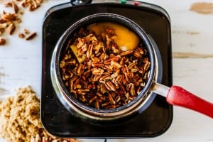 A saucepan with chopped pecans, butter, eggs, and brown sugar sits on a black stovetop—just the start of a delicious pecan pie dip. Nearby, a pile of brown sugar and scattered pecans hint at irresistible flavor.