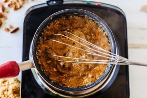 A pot of bubbling brown pecan pie dip is being stirred with a metal whisk on a stovetop.