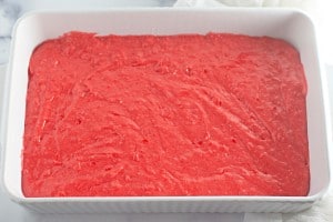 A white rectangular baking dish filled with an even layer of bright pink cake batter.