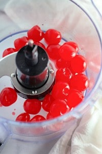 Red maraschino cherries inside a food processor bowl, ready to be processed.