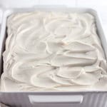 A rectangular white baking dish filled with a cake topped with thick, swirled white frosting.