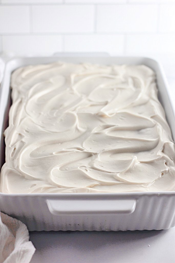 A rectangular white baking dish filled with a cake topped with thick, swirled white frosting.
