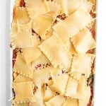 A baking dish filled with uncooked lasagna, topped with overlapping sheets of pasta and layered with sauce and cheese, viewed from above.