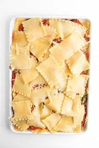 A baking dish filled with uncooked lasagna, topped with overlapping sheets of pasta and layered with sauce and cheese, viewed from above.