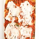 A baking dish filled with unbaked lasagna, showing layers of pasta, meat sauce, and ricotta cheese spread on top.