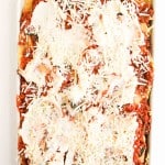 A baking dish filled with unbaked lasagna, topped with tomato sauce, shredded cheese, and ricotta cheese, ready to be cooked.