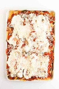 A baking dish filled with unbaked lasagna, topped with tomato sauce, shredded cheese, and ricotta cheese, ready to be cooked.