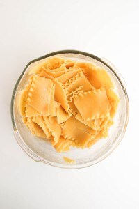 A glass bowl filled with cooked, broken lasagna noodles on a white surface.