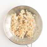 Chopped onions saut&eacute;ing in a stainless steel pan on a white background.