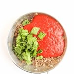 A frying pan with cooked ground meat, chopped spinach, and tomato sauce on a white background.