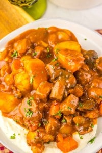 A plate of Slow Cooker Beef Bourguignon stew with potatoes, carrots, and mushrooms in a thick brown sauce served over mashed potatoes, garnished with chopped parsley.