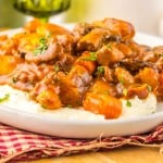 A plate of mashed potatoes topped with Slow Cooker Beef Bourguignon—a hearty stew of tender beef, carrots, mushrooms, and a garnish of chopped herbs.