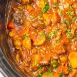 Close-up of Slow Cooker Beef Bourguignon with potatoes, carrots, and garnished with chopped parsley in a slow cooker.
