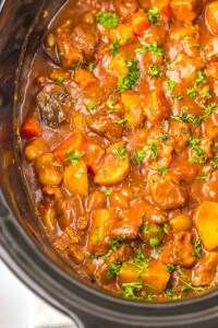 Close-up of Slow Cooker Beef Bourguignon with potatoes, carrots, and garnished with chopped parsley in a slow cooker.
