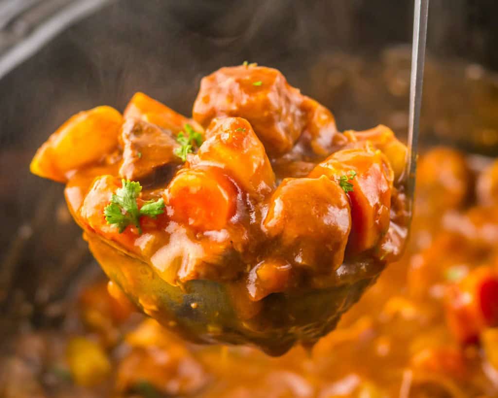 A ladle lifting a serving of Slow Cooker Beef Bourguignon, showcasing chunks of meat, potatoes, carrots, and a parsley garnish.