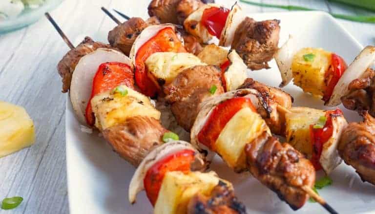 Grilled meat and vegetable skewers with chunks of pineapple, onion, and red bell pepper served on a white plate.