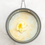 A saucepan containing milk and a chunk of butter on a light-colored marble surface, ready to create the rich frosting for a classic German Chocolate Bundt Cake.