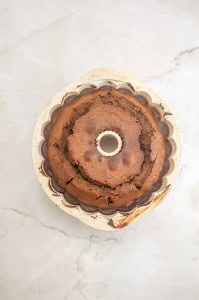 A freshly baked German Chocolate Bundt Cake sits in a fluted ceramic pan on a light-colored marble surface.