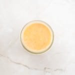 A glass filled with light orange juice sits on a white marble surface, viewed from above—its brightness reminiscent of the golden tones found in a freshly baked German Chocolate Bundt Cake.