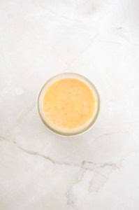 A glass filled with light orange juice sits on a white marble surface, viewed from above—its brightness reminiscent of the golden tones found in a freshly baked German Chocolate Bundt Cake.