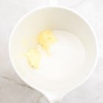 White mixing bowl with two dollops of butter and a pile of granulated sugar, ready to be mixed for a delicious German Chocolate Bundt Cake, placed on a light marble surface.