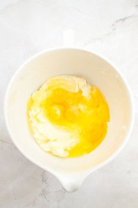 A white mixing bowl containing flour and cracked raw eggs on a light marble surface, ready for creating a delicious German Chocolate Bundt Cake.