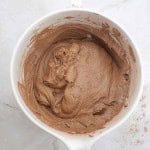 A white mixing bowl filled with creamy, light brown German Chocolate Bundt Cake batter sits on a marble surface.