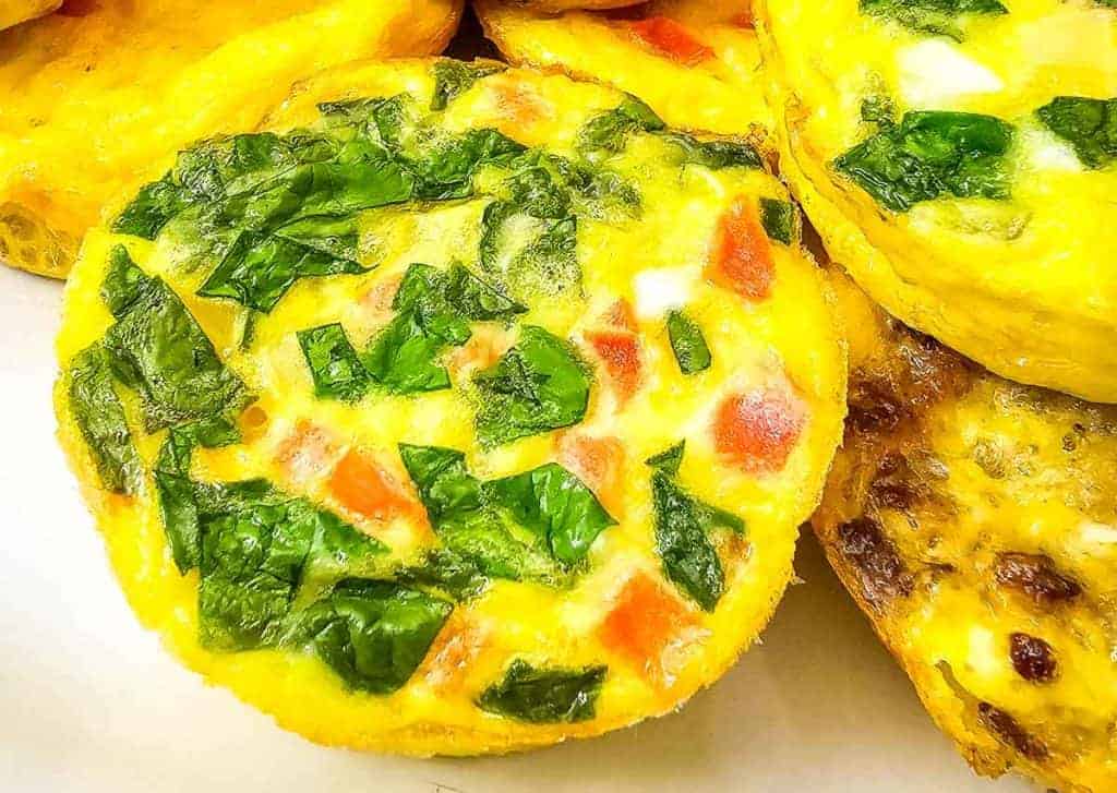 Close-up of a baked egg muffin topped with chopped spinach, diced tomatoes, and bits of white cheese—a delicious choice for those searching for easy egg recipes.
