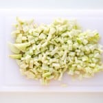 Chopped pieces of pale green vegetable on a white cutting board.