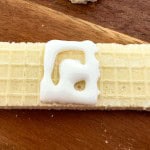 A rectangular vanilla wafer cookie with a small amount of white icing on top, placed on a wooden surface.