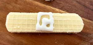A rectangular vanilla wafer cookie with a small amount of white icing on top, placed on a wooden surface.
