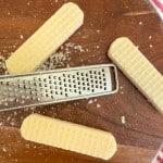 Four rectangular wafer cookies and a metal grater on a wooden surface, with crumbs scattered around.