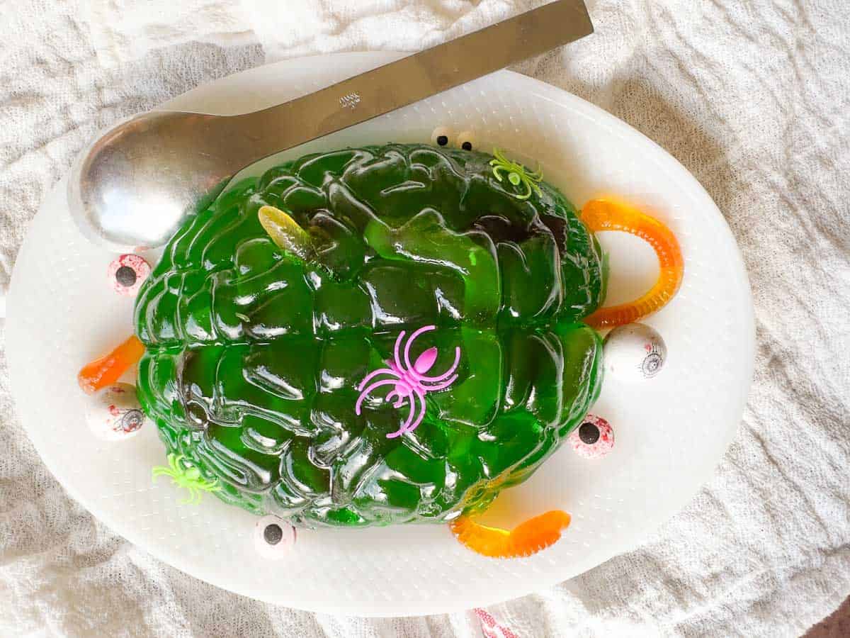 Green gelatin mold shaped like a brain with gummy worms and candy eyeballs for decoration.
