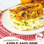 Grilled apple and brie stuffed chicken breast served on mashed potatoes, garnished with parsley, on a white plate with an apple and drink in the background.