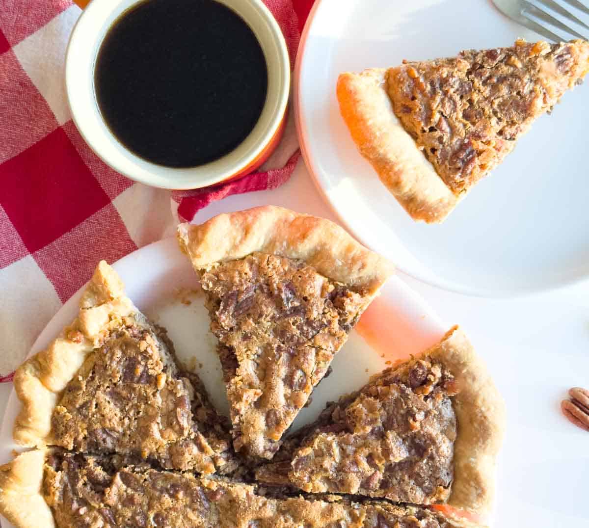 A sliced chopped pecan pie on a white plate, with one slice served on a separate plate beside a cup of black coffee on a red-and-white checkered cloth.