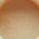 A close-up of a bowl filled with light brown batter, showing a smooth texture with small bubbles on the surface.
