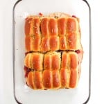 A glass baking dish filled with baked slider sandwiches made with golden brown rolls, sliced and arranged in rows.