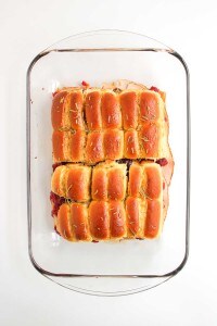 A glass baking dish filled with baked slider sandwiches made with golden brown rolls, sliced and arranged in rows.