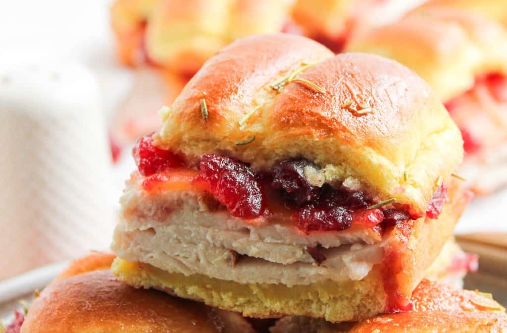 A close-up of a slider sandwich with layers of sliced turkey, cranberry sauce, and a soft golden bun.