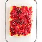 A glass baking dish containing layered slices of cheese and meat, topped with a red cranberry sauce.