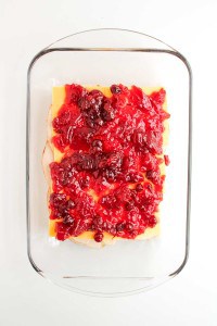 A glass baking dish containing layered slices of cheese and meat, topped with a red cranberry sauce.