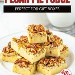 A plate of pecan pie fudge squares topped with chopped pecans, stacked on a white plate, with a glass of milk in the background for the perfect pecan pie fudge treat.