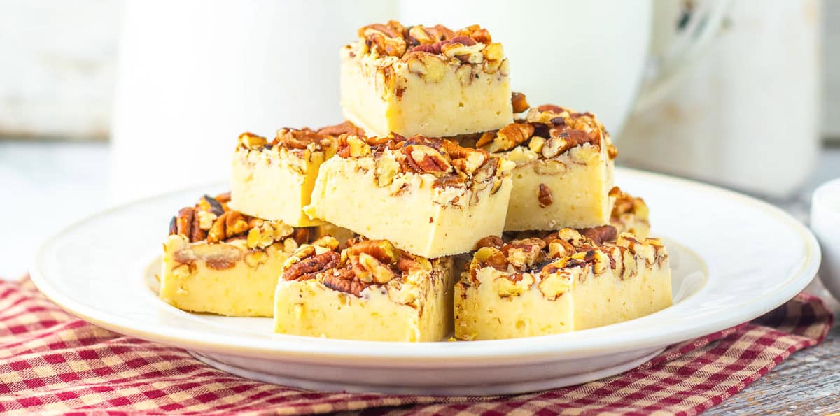 Stacked squares of creamy pecan pie fudge topped with chopped pecans on a white plate.