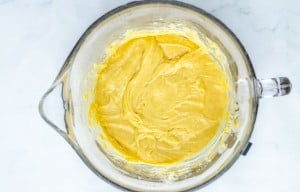 A glass mixing bowl filled with yellow cake batter sits on a white surface.