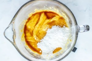 A glass mixing bowl containing a yellow batter with a mound of white powdered sugar on top, ready to be mixed.