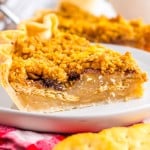 A slice of double-layer pie with a crumb topping sits on a white plate, showing layers of filling and crust, with a red checkered cloth underneath.