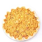 A baked pie with a golden brown crumb topping in a clear glass pie dish, photographed from above on a white background.